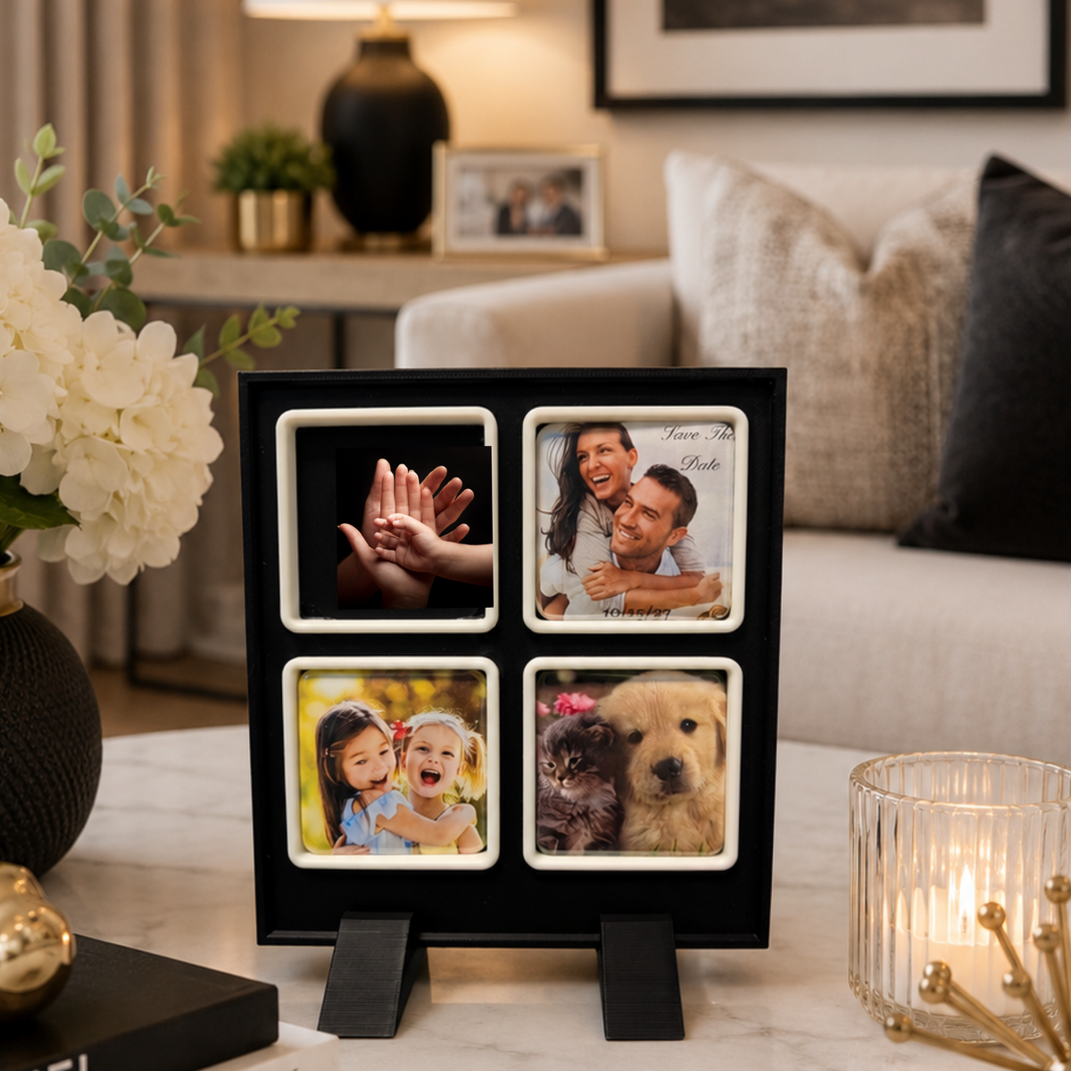A black four-photo magnet frame with white borders and small black easel feet stands on a marble surface in a living room. The four slots contain sample photos: hands, a couple, children, and a dog.