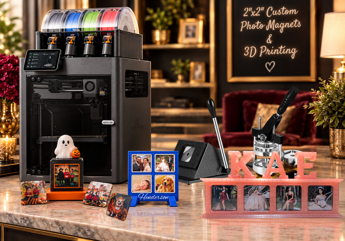 A 3D printer with colorful filament cartridges sits on a marble countertop in a decorated home office or studio, alongside custom photo magnets, a small ghost figure, a blue nameplate, and a pink photo frame. A chalkboard in the background reads '2x2 Custom Photo Magnets & 3D Printing'.