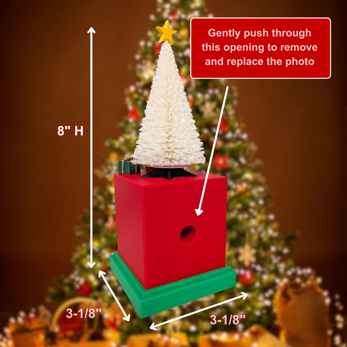 A small Christmas tree decoration or gift box with a white textured tree on top, shown with dimension labels (8" high, 3-1/8" by 3-1/8" base) and a red callout box explaining how to remove the top photo. The background is a blurred Christmas tree in warm brown tones.