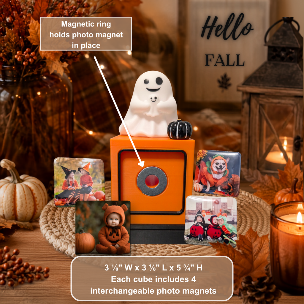 An orange decorative photo cube display with a white ghost figure on top, surrounded by four sample square photo magnets and a text callout explaining that the magnetic ring holds the photo magnet in place. The scene is styled in autumn with pumpkins, candles, and fall decor.