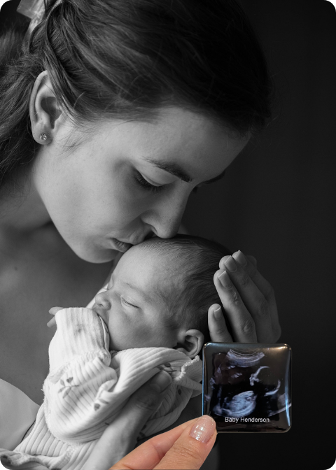 Black and white photo of a mother holding her newborn, with a hand holding an ultrasound photo magnet.