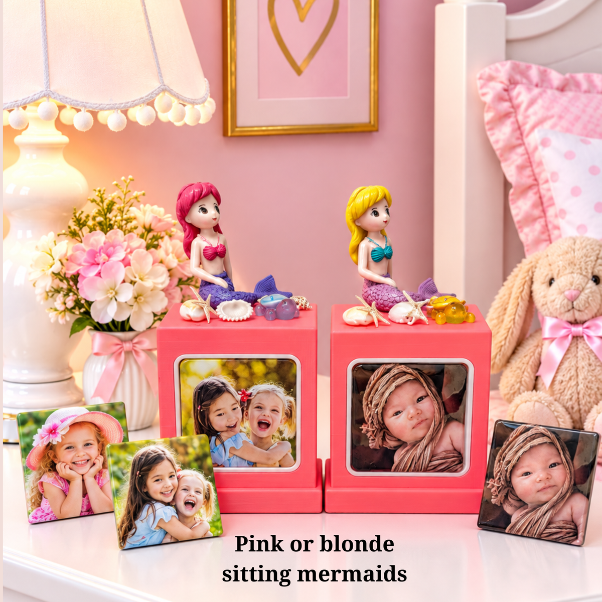 A pink memory cube photo frame stand set styled in a nursery, featuring two square pink frames with mermaid figurines on top and two custom photo inserts. The text overlay reads 'Pink or blonde sitting mermaids'.