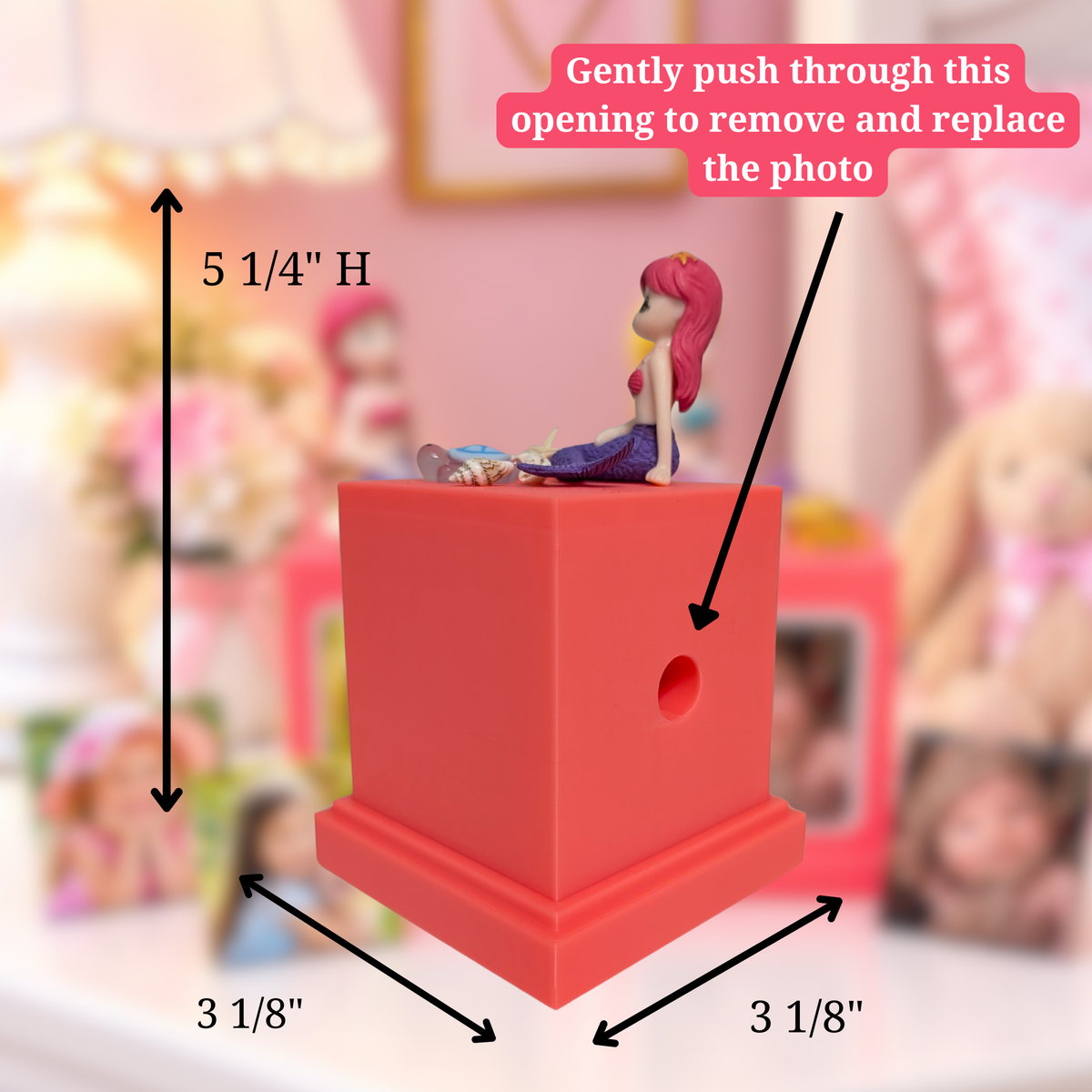 A pink memory cube photo display with a mermaid figurine sitting on top, shown with black dimension arrows and text labels indicating 3 1/8" by 3 1/8" by 5 1/4"H " dimensions. A pink text bubble says to gently push through an opening to remove and replace the photo.