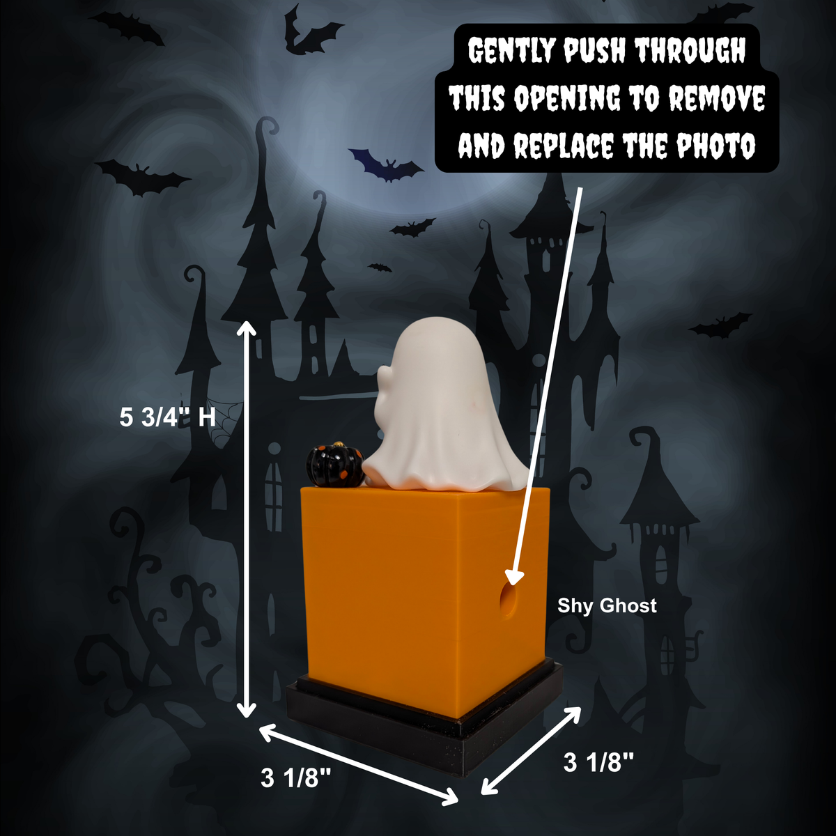 A Halloween ghost figurine sitting on an orange photo frame display with a black base, labeled with dimensions (5 3/4" high, 3 1/8" wide by 3 1/8" deep) and instructions on how to replace the photo, over a spooky haunted-house background.