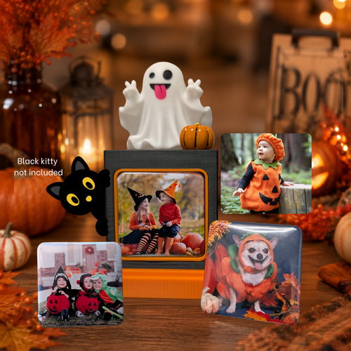 A Halloween-themed photo display with a white silly ghost,  an orange little pumpkin, three photo magnets arranged on a wooden table. A black cat element print not included.