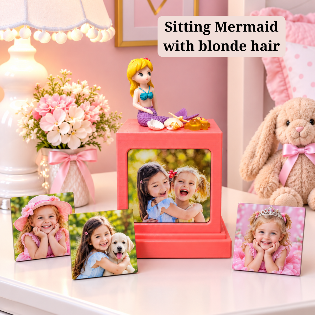 A pink memory cube photo display stand with a mermaid figurine on top, shown in a styled room scene with three photo magnets and a photo magnet inside the cube. Text overlay reads 'Sitting Mermaid with blonde hair'.
