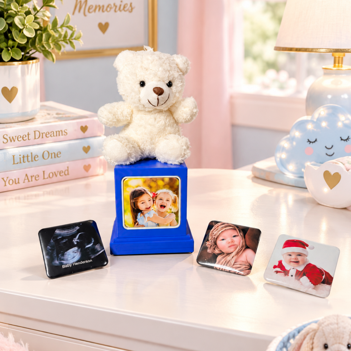 A personalized photo display set on a white tabletop in a softly styled room. A white teddy bear sits on a blue memory cube with three photo magnets displayed around it. 